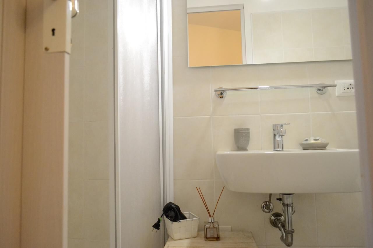 A bathroom with a white sink, a mirror above it, and a towel rack. There is a small bottle of soap and a glass container on the sink.