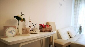 A hotel room with a white desk, a vase with flowers, a candle, a basket with red items, and a beige sofa. - Casa Isabella (Verona)
