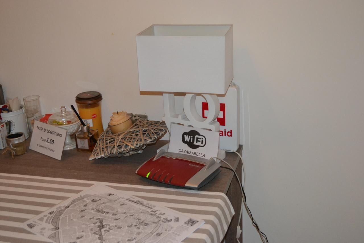 Une table avec un routeur Wi-Fi, un panneau indiquant un coût de 1,50 euro pour l’accès Wi-Fi, une tasse de café, un panier et un journal.