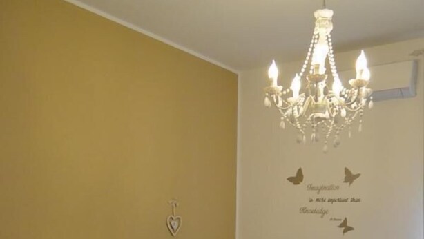 A hotel room with two beds, a chandelier, a heart-shaped decoration, and a motivational quote on the wall. - Casa Isabella (Verona)