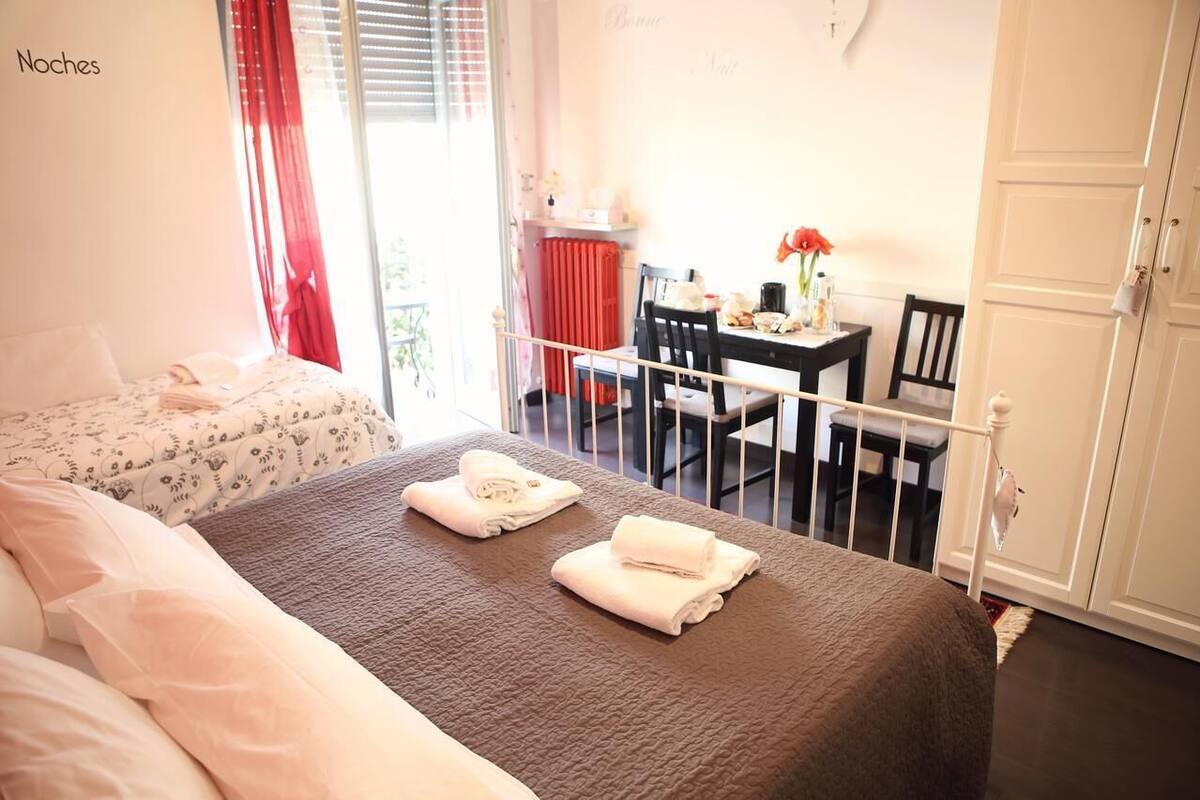 A bedroom with a bed, a small table with a chair, and a window with curtains.