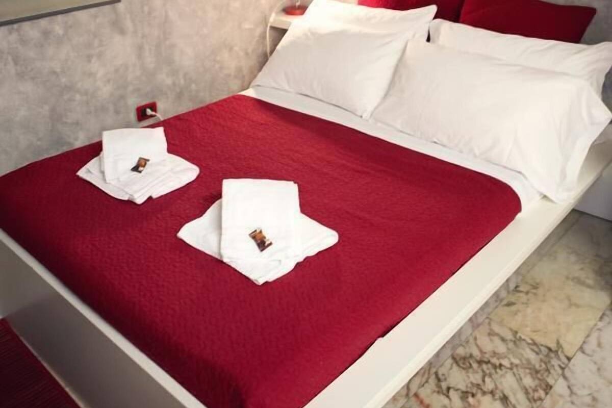 A neatly made bed with red and white bedding, a nightstand with a lamp, and a wall with a partial quote.