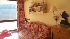 A cozy room with a wooden sofa, a small table, a lamp, and a shelf with books and a lighthouse decoration.