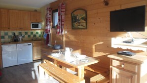 A wooden cabin-style kitchen with wooden cabinets, a microwave, a sink, and a dining area with benches and a table.