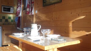 A wooden interior with a wooden table set for dining, a bench, a microwave, and a painting on the wall.