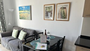 Ein Wohnbereich mit grauem Sofa, zwei gerahmten Bildern, einem Esstisch mit Stühlen, einer Wasserflasche und einer Speisekarte.