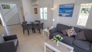 A modern living room with a grey sofa, patterned chairs, a coffee table, and a painting of the sea.