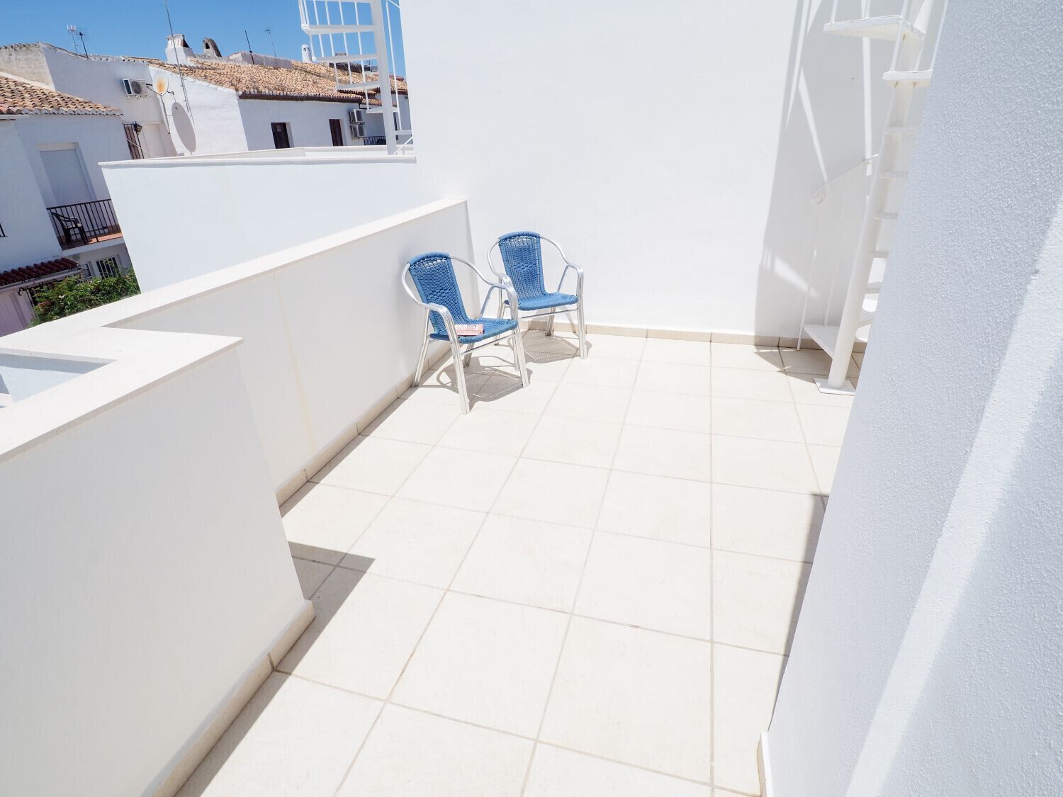 Ein Balkon mit zwei blauen Stühlen, weißen Wänden und einem gefliesten Boden.