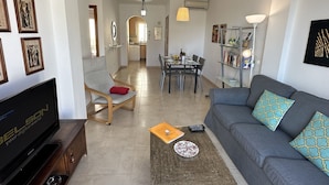 A modern living room with a grey sofa, a television, and a dining area with a table and chairs. - Nerja Paradise Rentals - Apartment Chimenea A1E (Nerja)