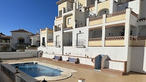 A pool area with a rectangular pool, surrounded by a white building with balconies and a tiled deck. - Nerja Paradise Rentals - Apartment Chimenea A1E (Nerja)