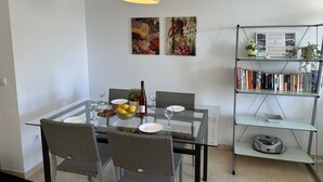 A modern dining area with a glass table, wicker chairs, a wine bottle, and a fruit bowl. - Nerja Paradise Rentals - Apartment Chimenea A1E (Nerja)