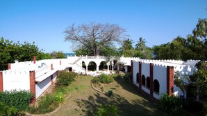 Un bâtiment blanc agrémenté de détails en briques rouges, avec une cour intérieure dotée d’arcades et d’un grand arbre.