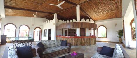 A spacious lounge area with a high ceiling, wooden furniture, and a central bar.