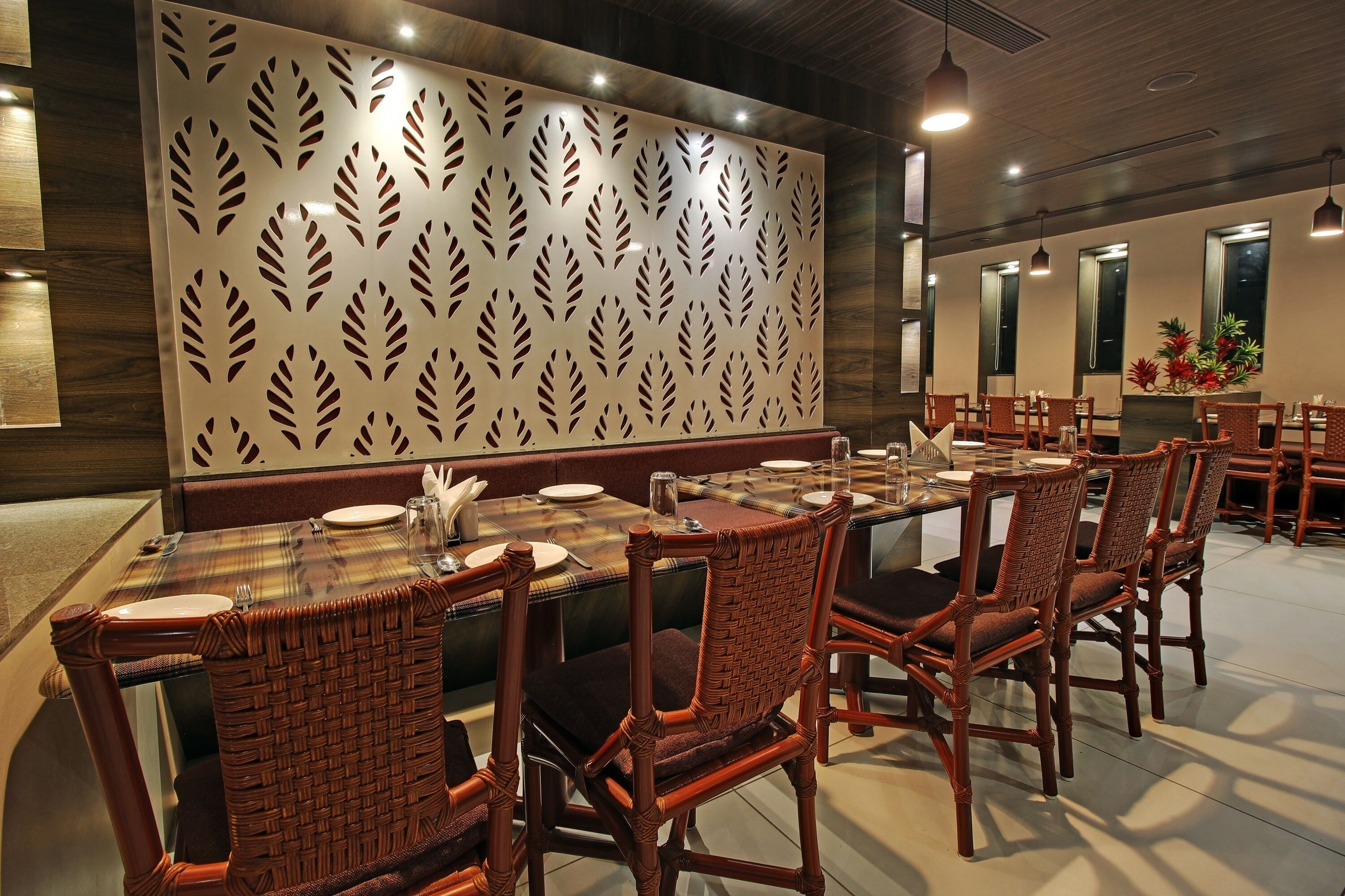 Un restaurante con una larga mesa dispuesta para comer, sillas de mimbre y una pared decorativa con motivos de hojas.