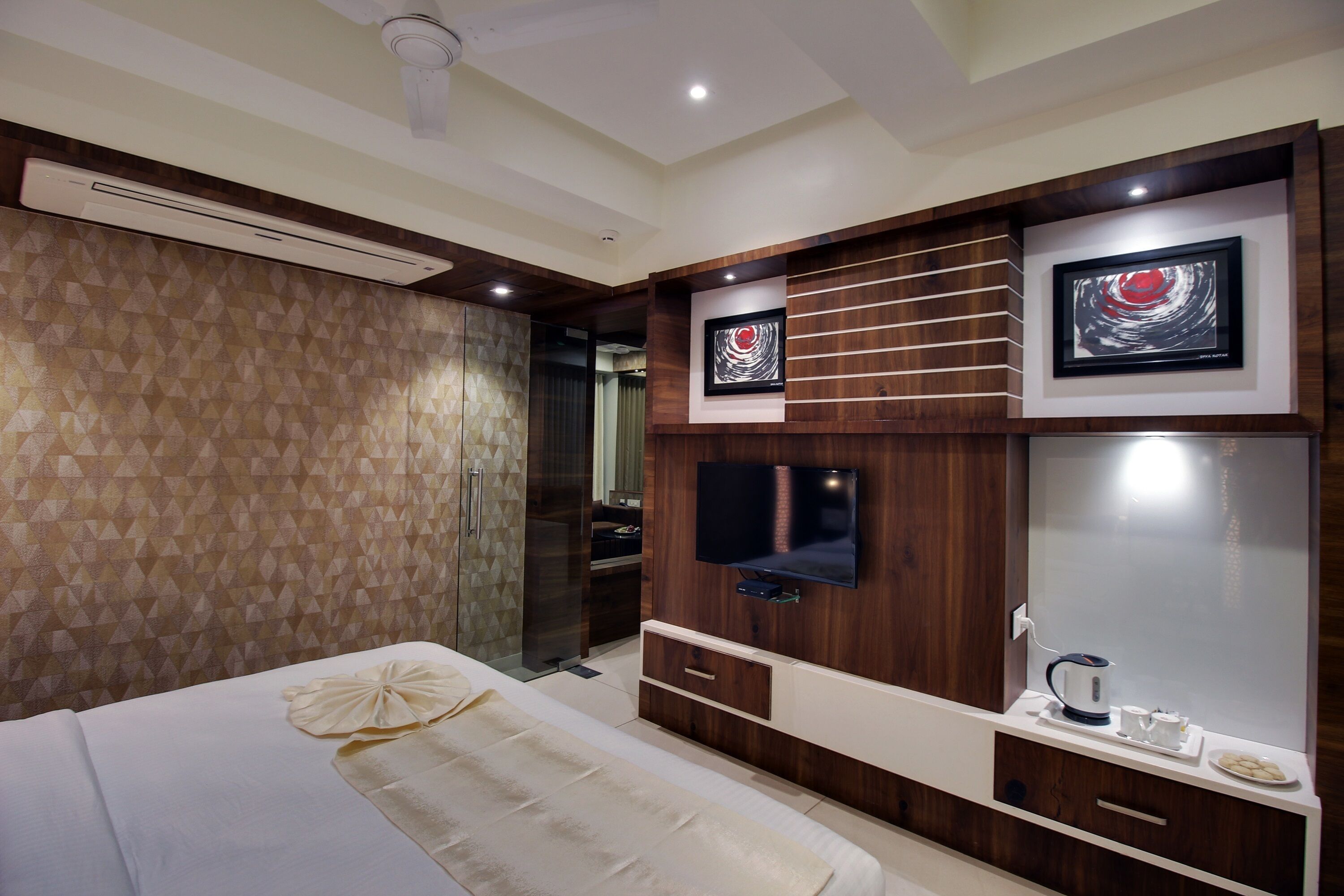 A hotel room with a bed, a TV mounted on the wall, a coffee maker, and artwork.