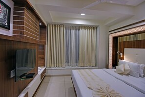 A modern hotel room with a large bed, a flat-screen TV mounted on the wall, and a window with curtains.