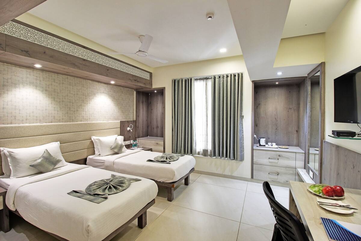A hotel room with two beds, a dining area, a TV, and a bathroom.