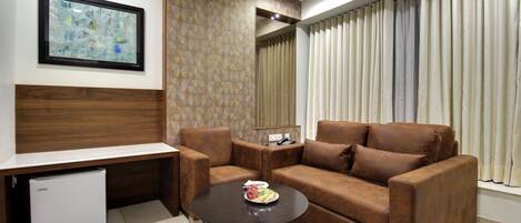 A modern living room with a brown leather sofa, a small coffee table, a white mini-fridge, and a framed abstract painting on the wall.