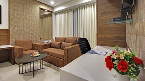 A modern living room with a brown sofa, a coffee table, and a white desk area. - SVASTI Inn Jamnagar (Jamnagar)