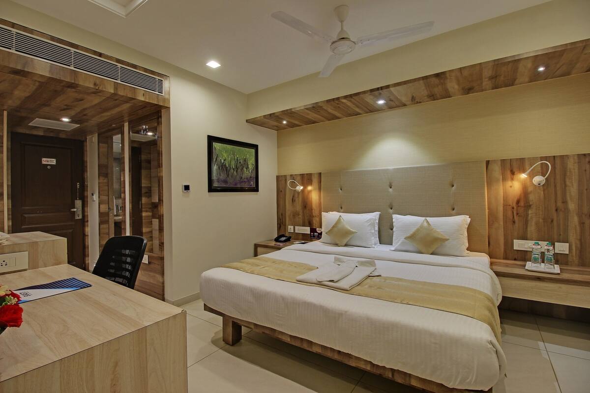 A hotel room with a large bed, wooden headboard, bedside tables, a desk, and a ceiling fan.