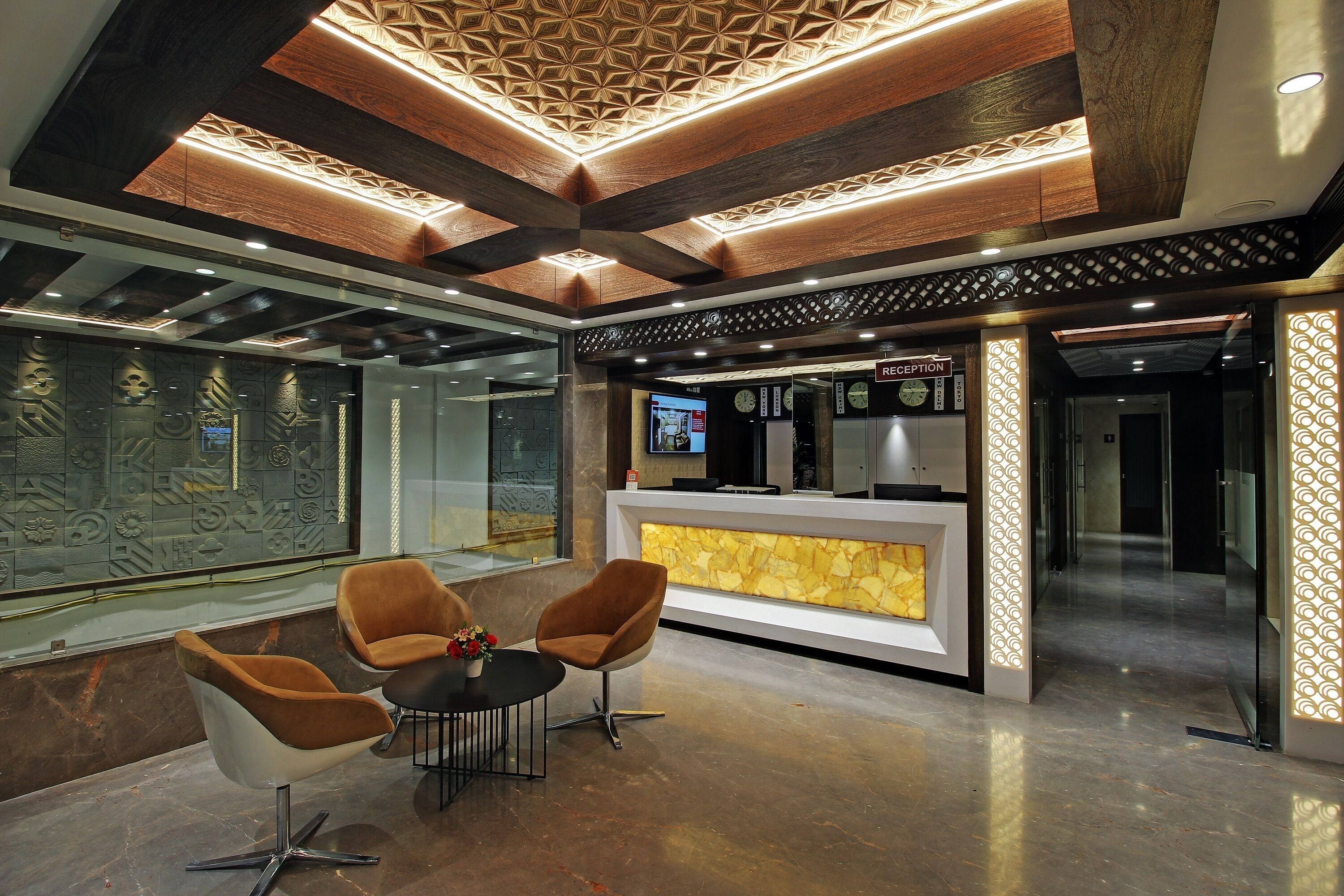 A reception area with a reception desk, two chairs, a small table with a vase, and a decorative wall with geometric patterns.
