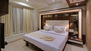 A hotel room with a large bed, a ceiling fan, a TV, and a mirror with decorative lighting. - SVASTI Inn Jamnagar (Jamnagar)