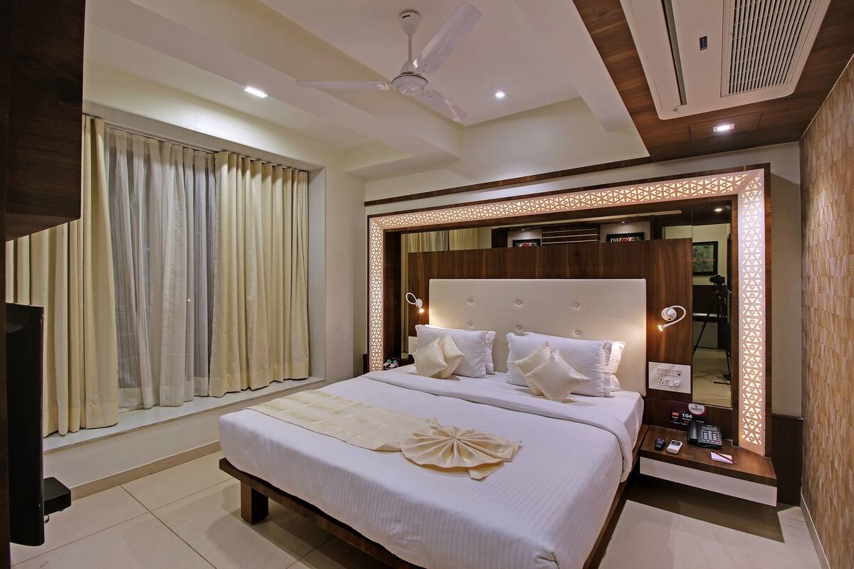 A hotel room with a large bed, a ceiling fan, a TV, and a mirror with decorative lighting.