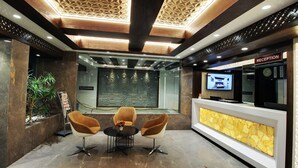 A reception area with a reception desk, a clock, and a television screen. - SVASTI Inn Jamnagar (Jamnagar)