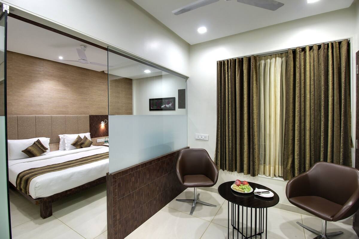 A hotel room with a bed, two chairs, a small table with a fruit plate, and a large window with curtains.