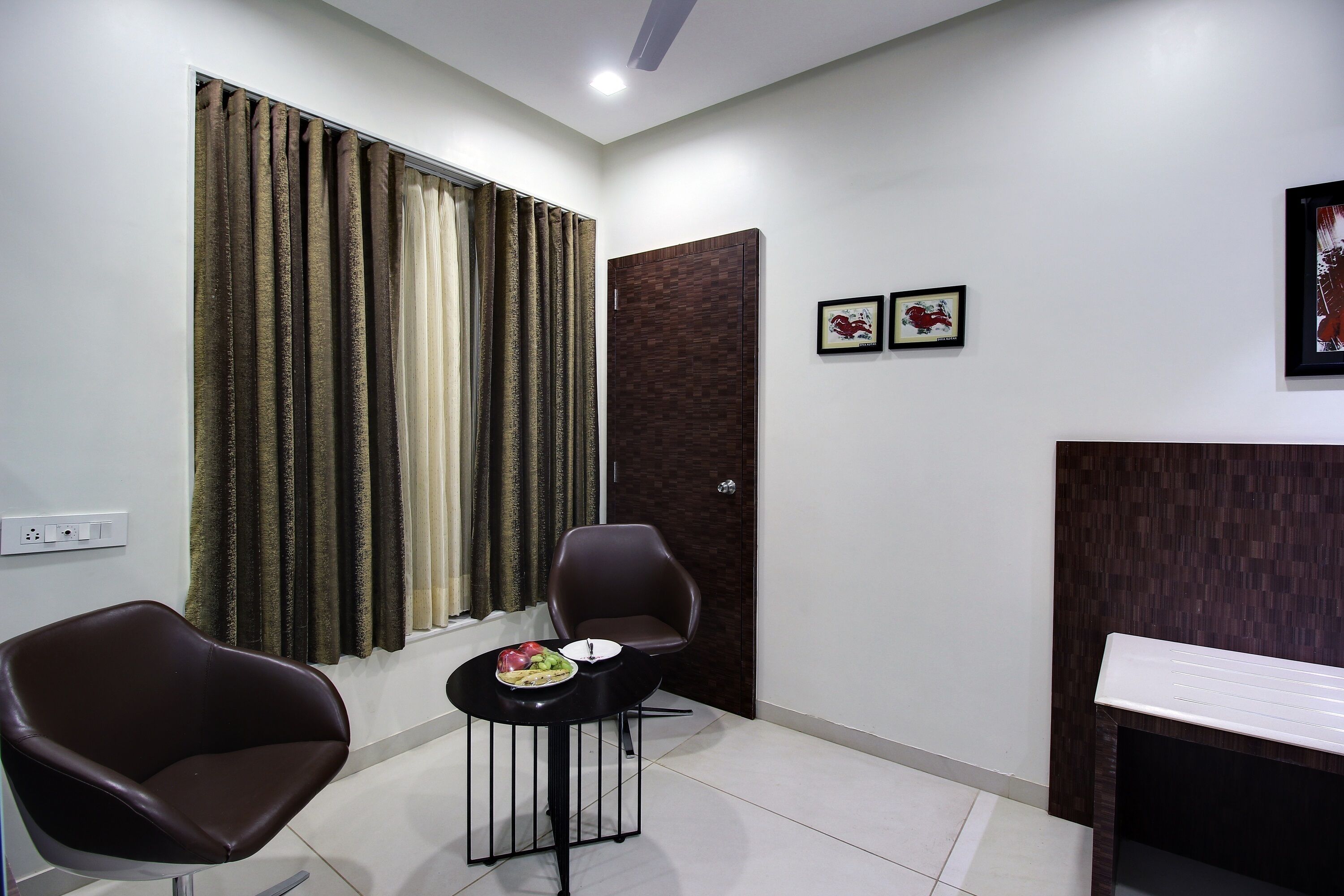 Una habitación moderna con una silla marrón oscuro, una pequeña mesa redonda con un frutero, y una puerta de madera oscura.