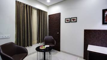Una habitación moderna con una silla marrón oscuro, una pequeña mesa redonda con un frutero, y una puerta de madera oscura.