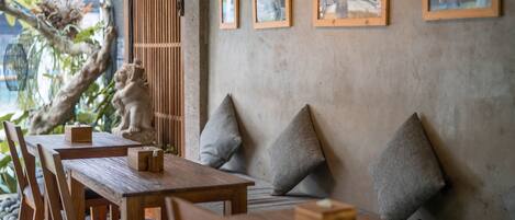 A restaurant interior with wooden tables and chairs, cushioned seating, and framed artwork on the walls.