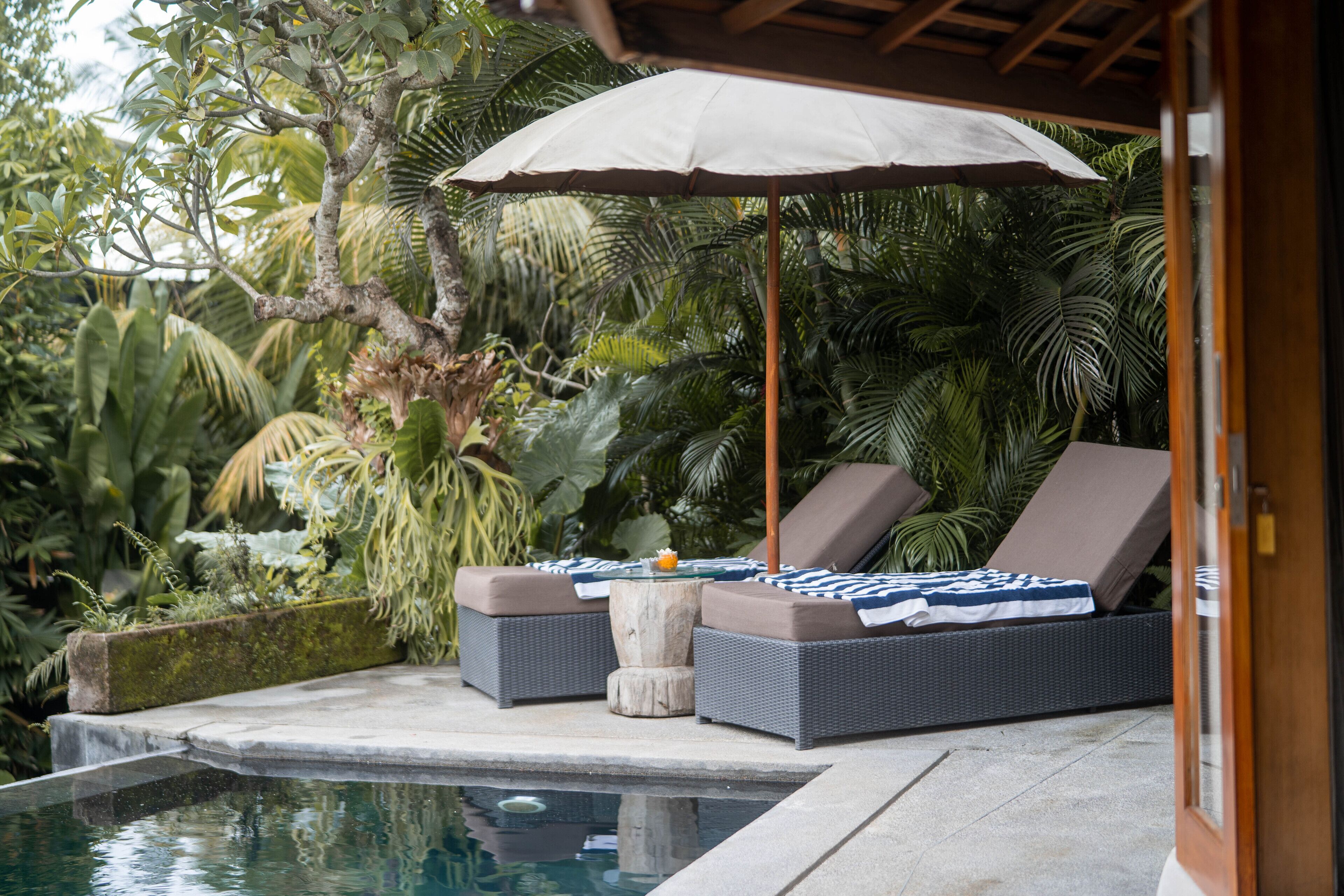 Un salon au bord de la piscine comprenant deux fauteuils confortables, une table et un grand parasol.