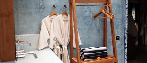 Un baño con un estante de madera con toallas y albornoces, un lavabo con grifería cromada y una pared azul con textura.