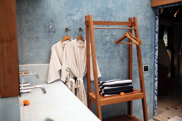 A bathroom with a wooden rack holding towels and robes, a sink with chrome fixtures, and a blue textured wall.