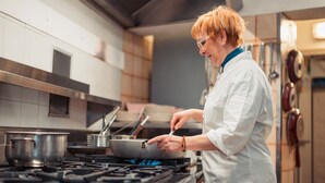 Una persona cocinando en una cocina con estufa a gas, ollas y campana extractora.