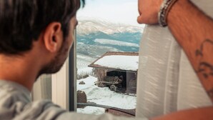 Una persona mirando por la ventana un paisaje nevado con un edificio y un carro.