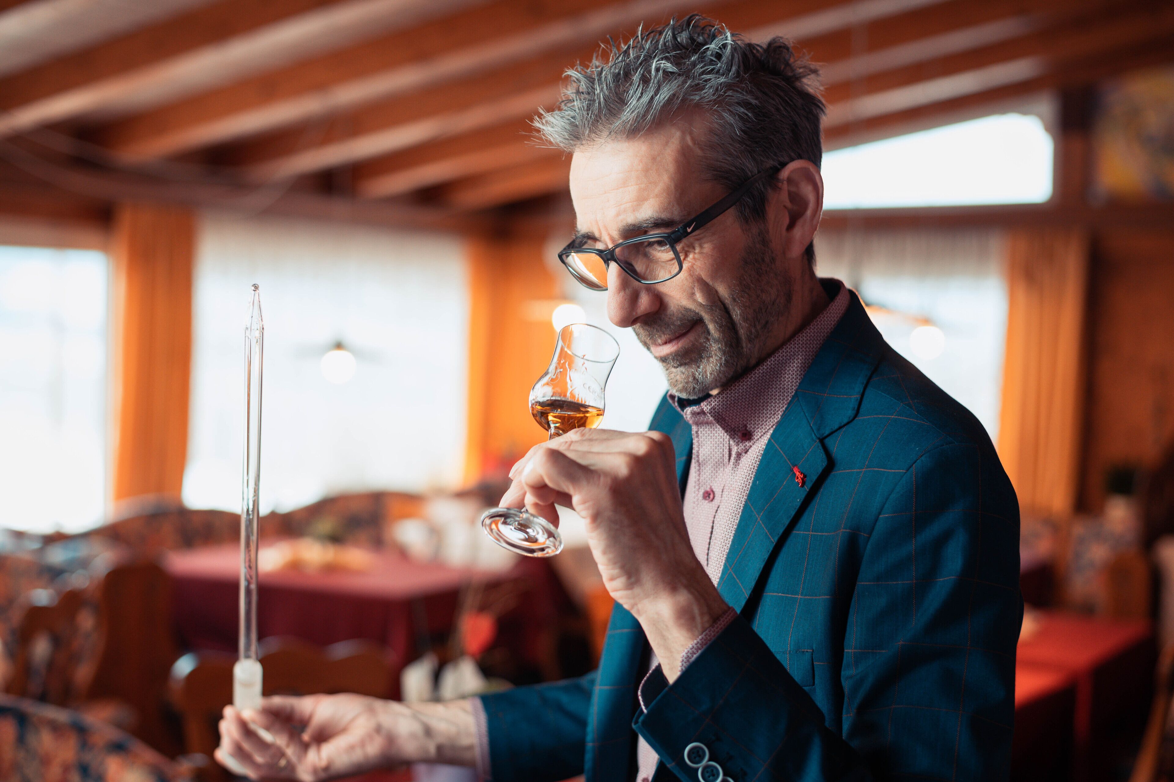 A person holding a wine glass and a thermometer, in a room with wooden beams and tables.