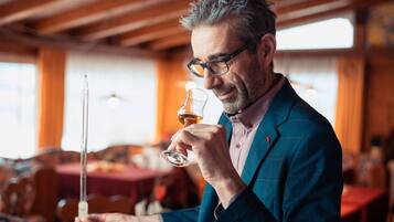 A person holding a wine glass and a thermometer, in a room with wooden beams and tables.