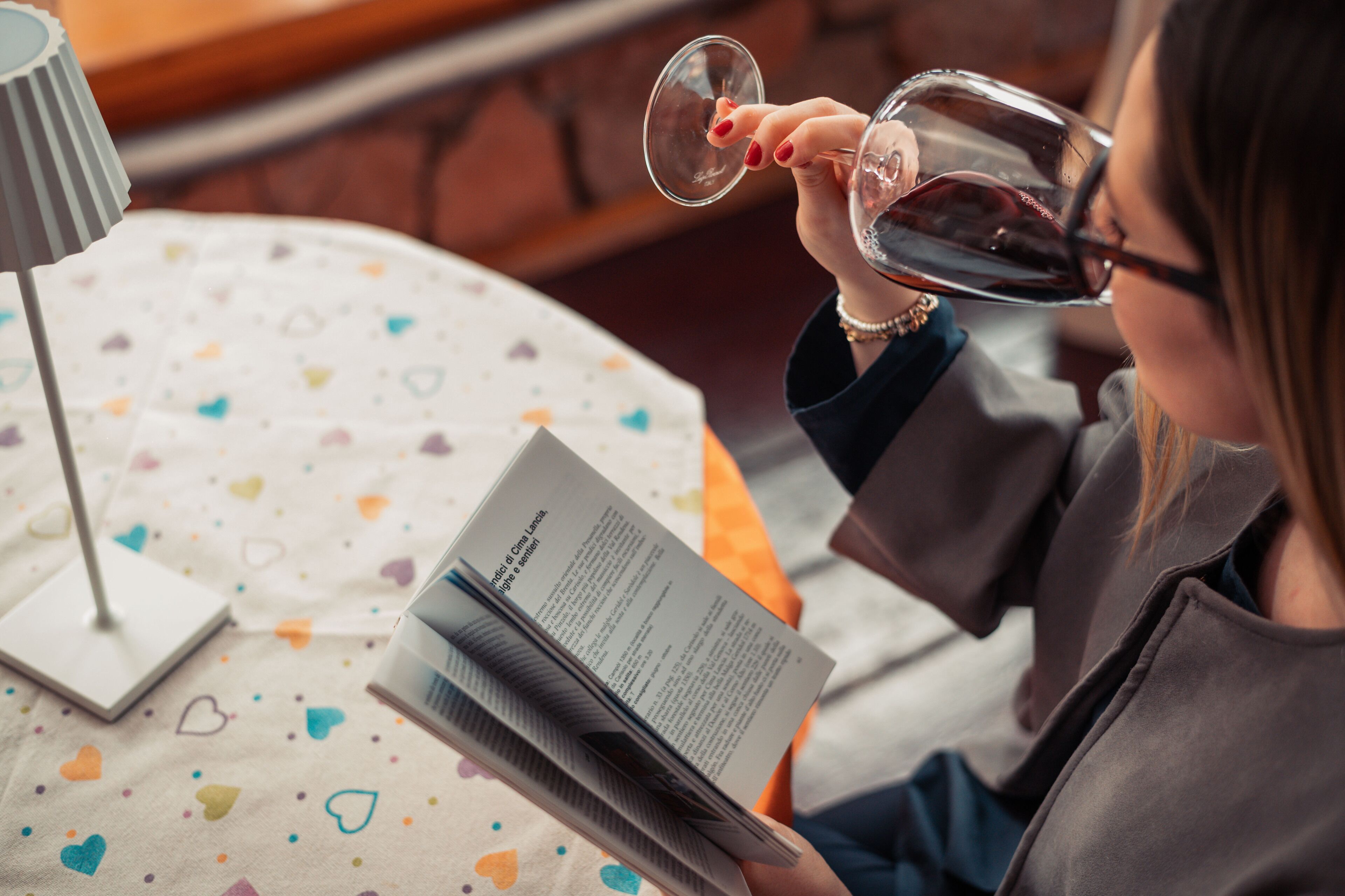 Una persona leyendo un libro en una mesa con mantel estampado.