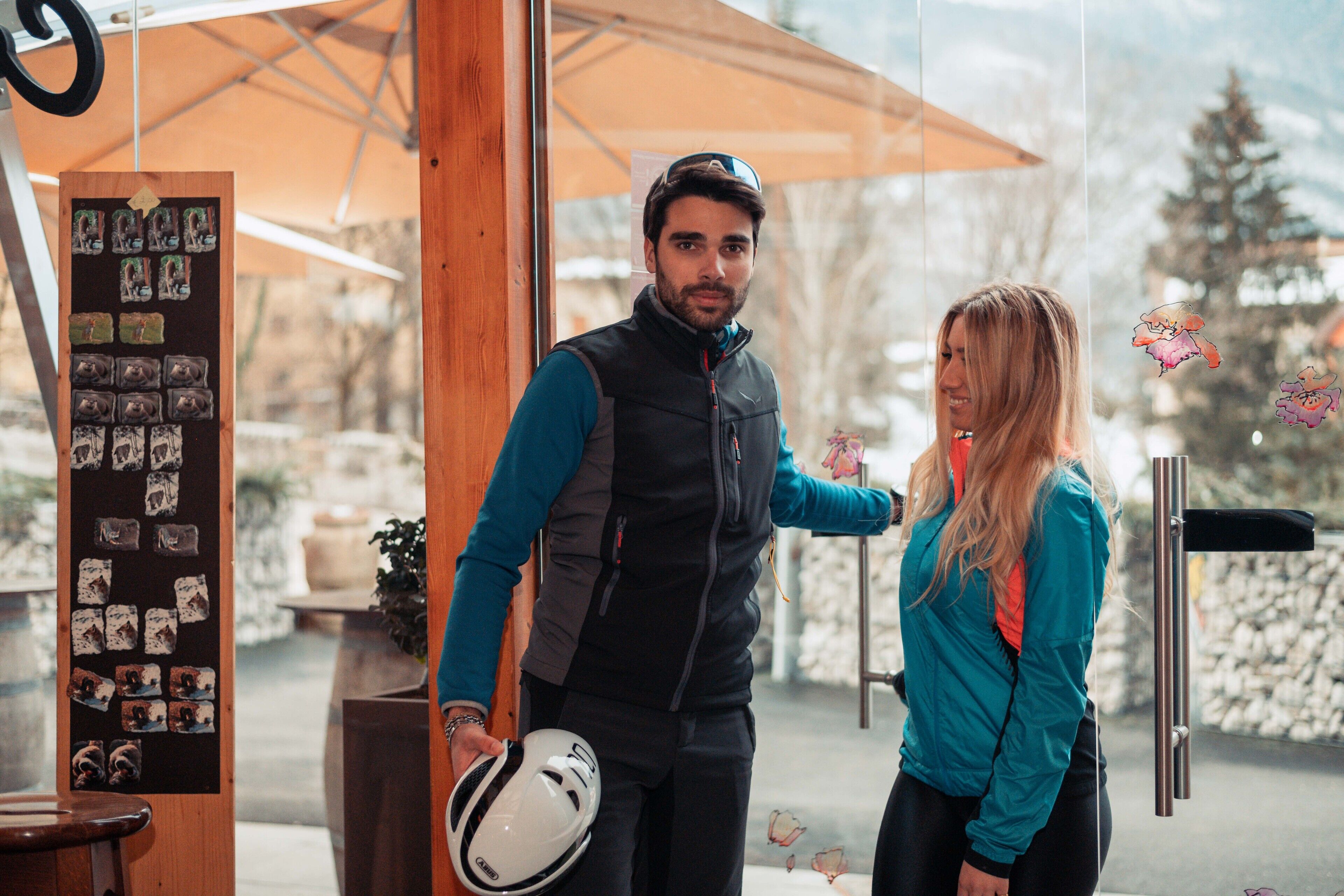A man holding a helmet, standing next to a woman in a teal jacket.