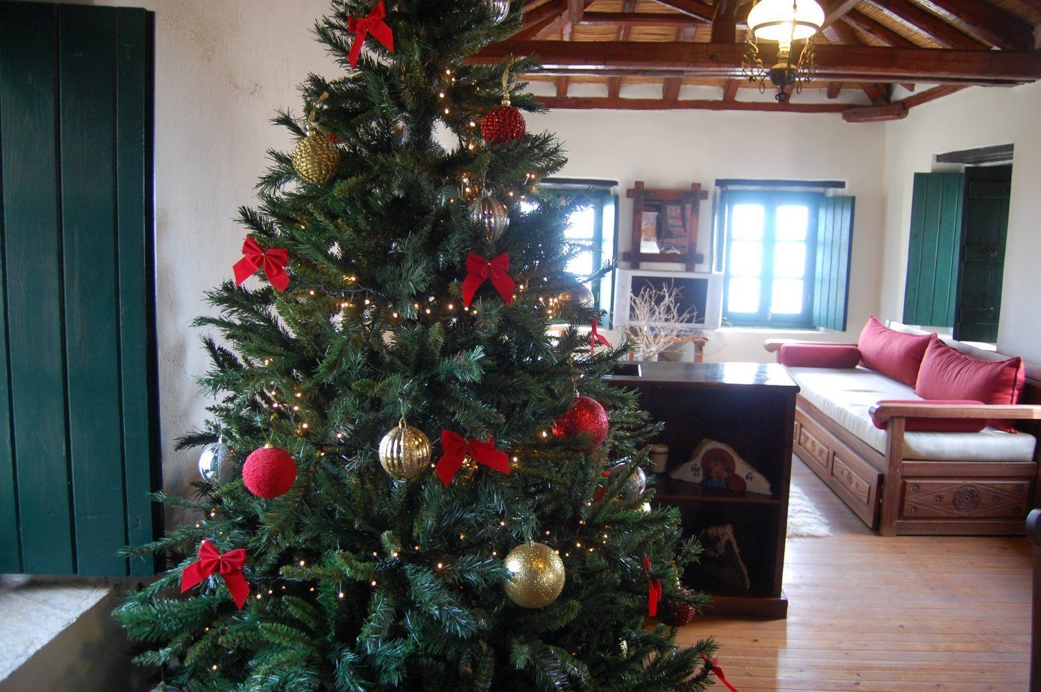 A cozy living room with a decorated Christmas tree, wooden furniture, and a rustic ceiling.