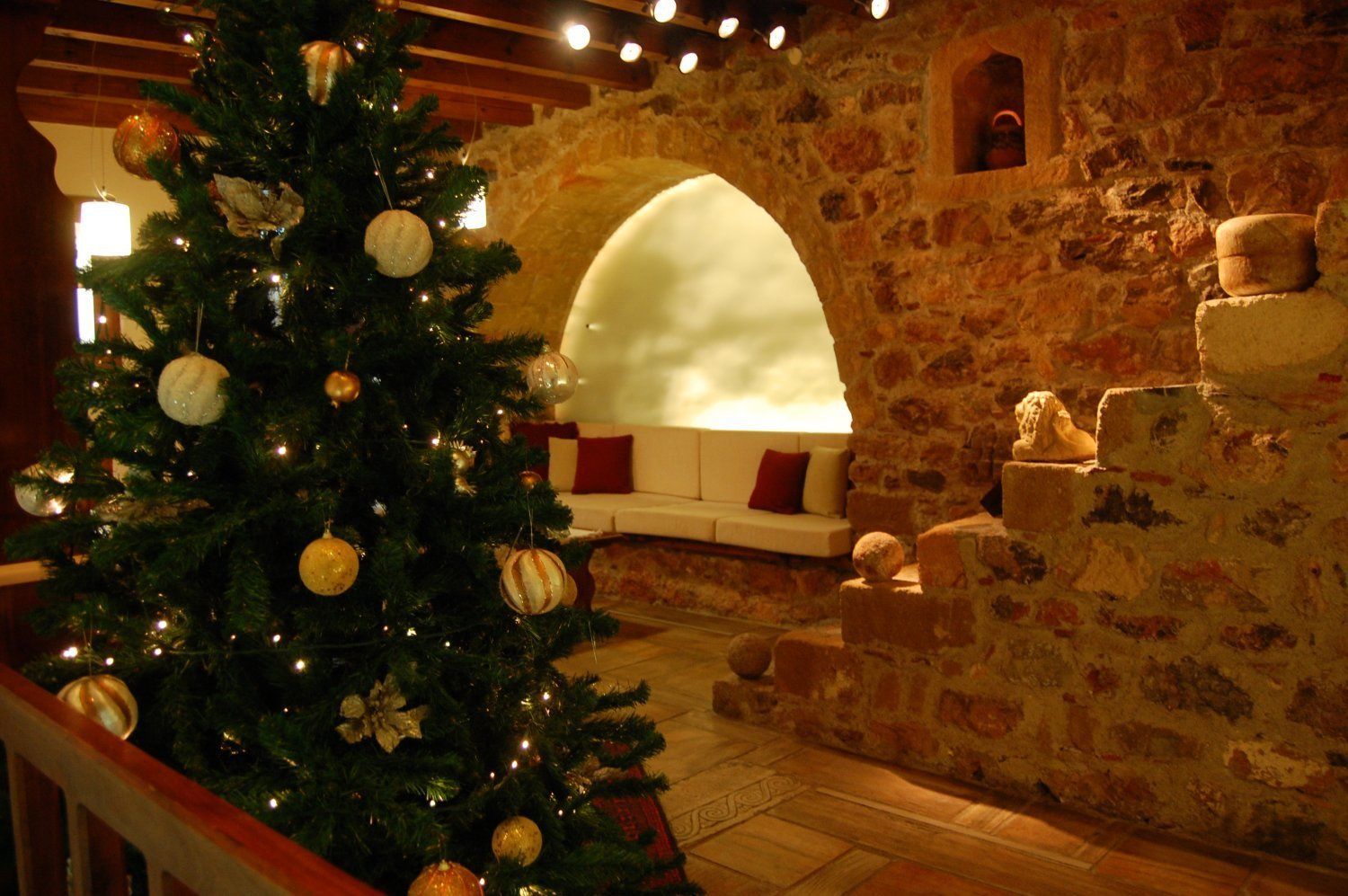 A Christmas tree with ornaments in a stone-walled room with a white sofa and a stone fireplace.