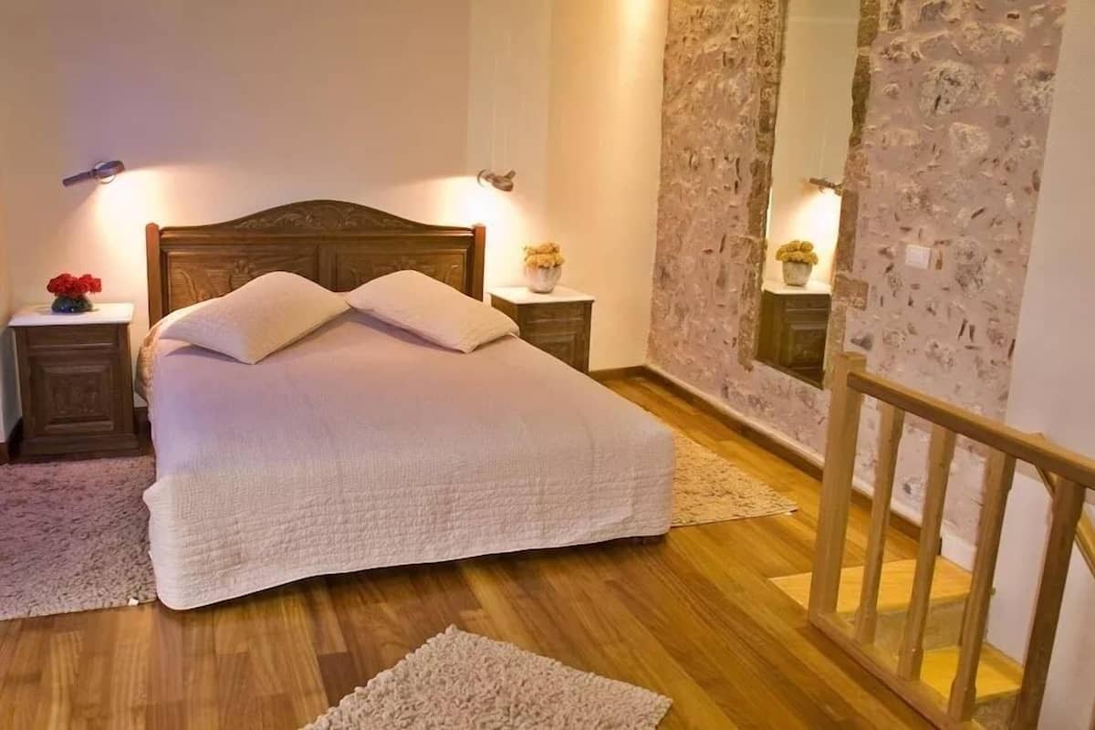 A neatly made bed with a wooden headboard, two bedside tables with lamps, and a stone wall with a mirror.