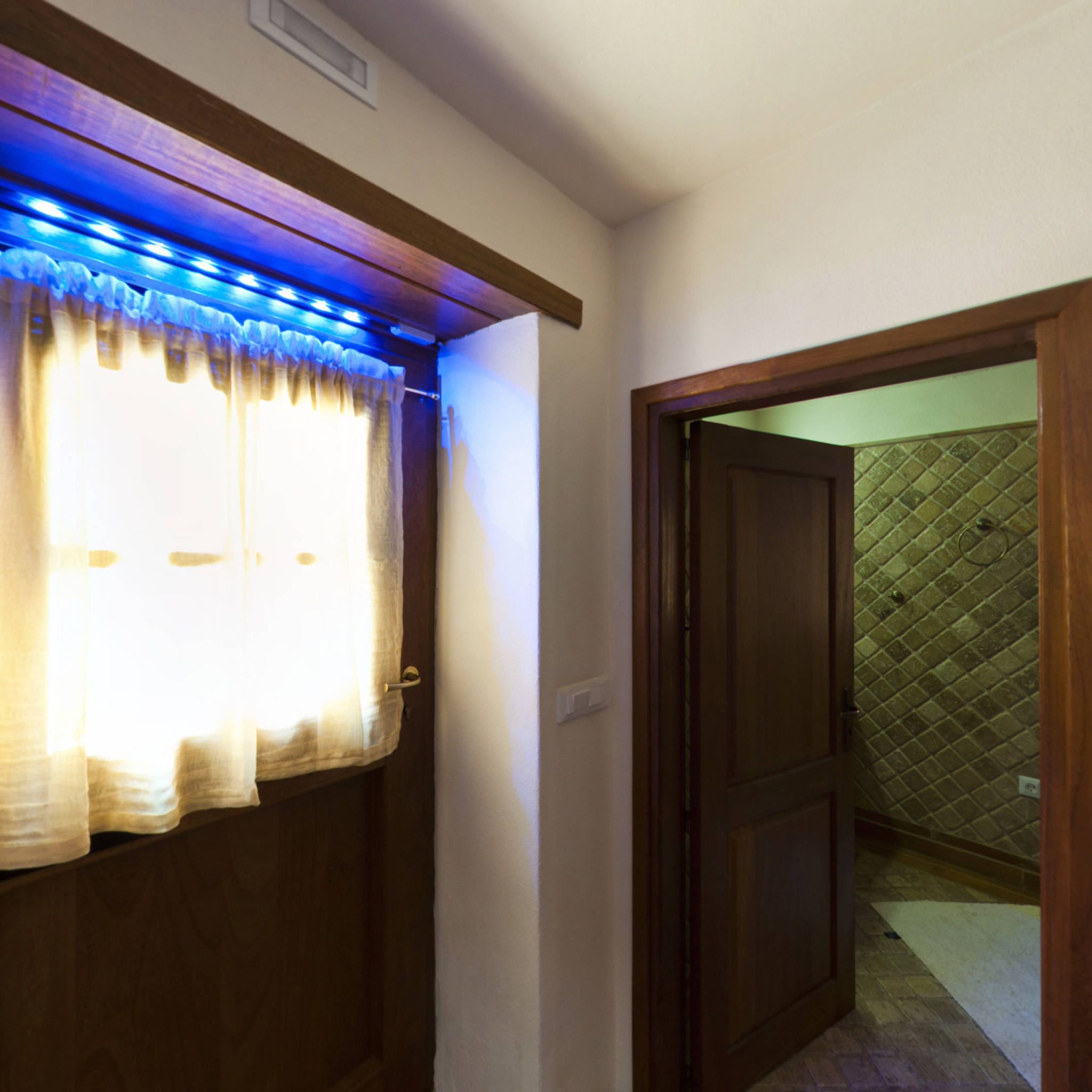 A hallway with a wooden door leading to a room with a tiled wall.