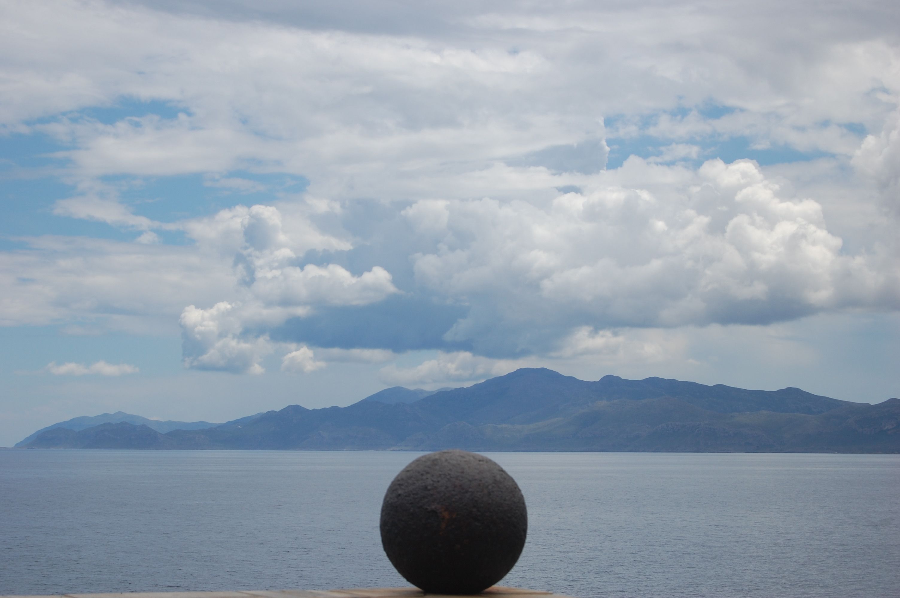 A large, spherical stone in the foreground with a calm body of water and mountains in the background.