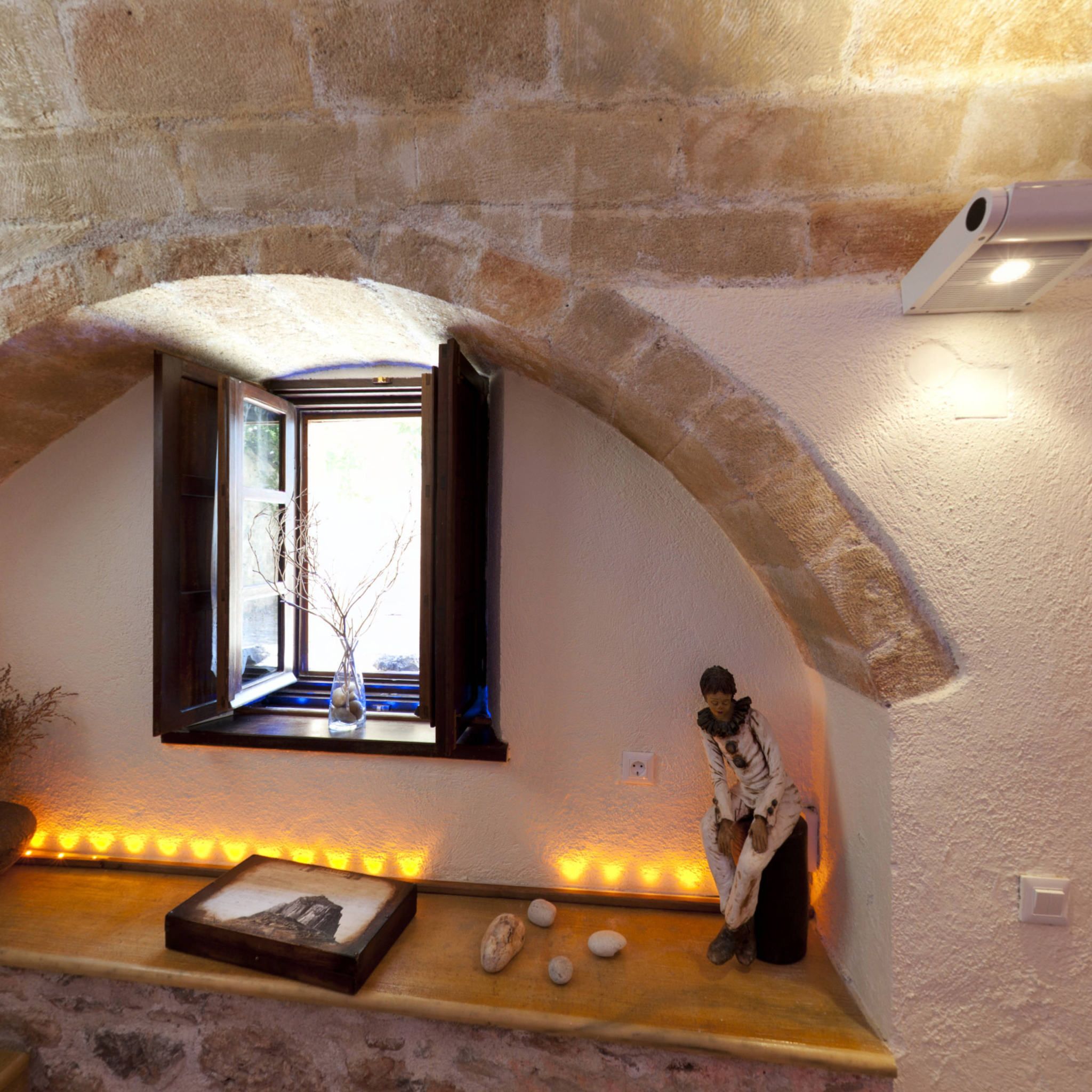 Une pièce chaleureuse avec un mur en pierre, une petite fenêtre donnant sur un beau paysage, une étagère ornée d’objets décoratifs et un radiateur fixé au mur.