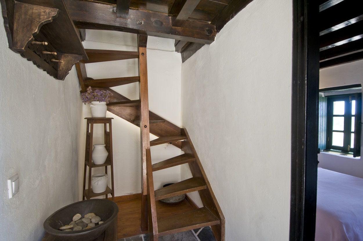 A wooden spiral staircase in a narrow room with white walls, a white door, and a window.