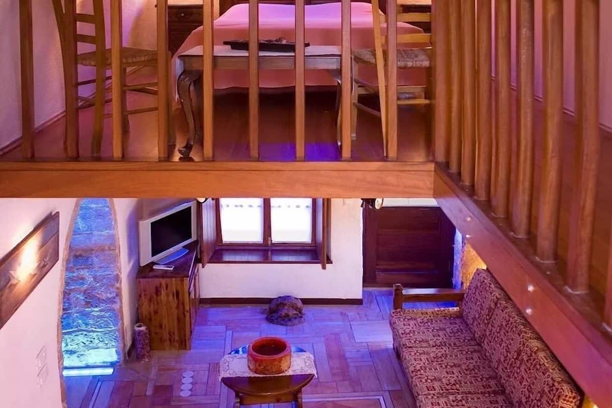A cozy loft-style room with a wooden balcony, a sofa, a television, and a small table with a decorative item.