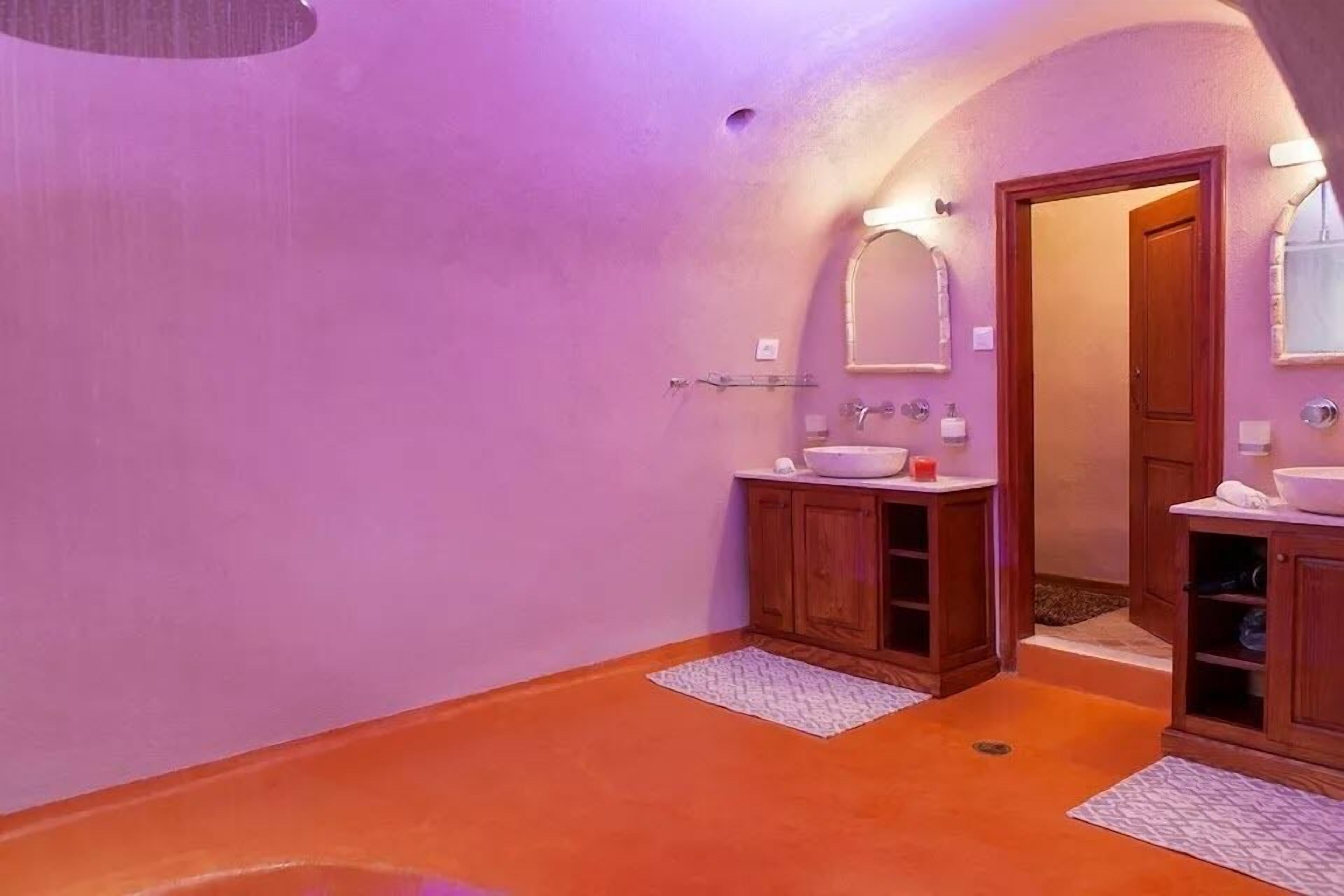 A bathroom with a purple wall, wooden cabinets, a sink, and a mirror.